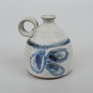 May include: A white ceramic pitcher with a blue and white abstract design. The pitcher has a handle and a rounded body.
