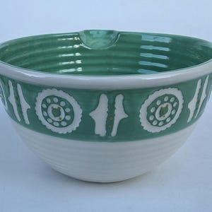 Peut inclure: Un saladier en c&eacute;ramique avec une base blanche et un bord et une bande d&eacute;corative vert teal. La bande pr&eacute;sente des motifs floraux et verticaux blancs. Le bol a un bec verseur et convient &agrave; la cuisine.