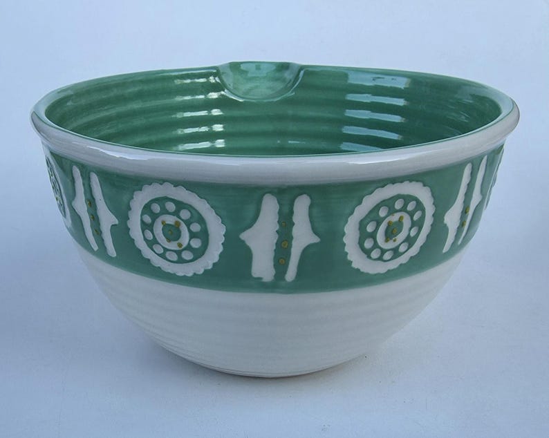 Peut inclure: Un saladier en c&eacute;ramique avec une base blanche et un bord et une bande d&eacute;corative vert teal. La bande pr&eacute;sente des motifs floraux et verticaux blancs. Le bol a un bec verseur et convient &agrave; la cuisine.