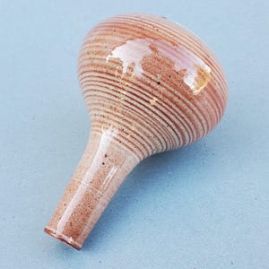 May include: A small, brown and white ceramic vase with a rounded bulbous top and a long, thin neck. The vase has a textured, striped pattern.