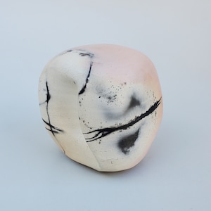 May include: A white ceramic sculpture with black and gray abstract markings. The sculpture is shaped like a rounded rock and has a pink hue.