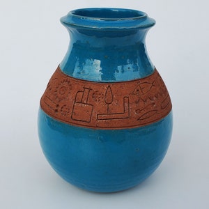 May include: A turquoise ceramic vase with a brown band around the middle. The band is decorated with a pattern of geometric shapes and symbols.