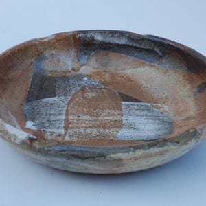 May include: A ceramic bowl with a white, brown, and gray glaze. The bowl has an irregular shape and a slightly raised rim.