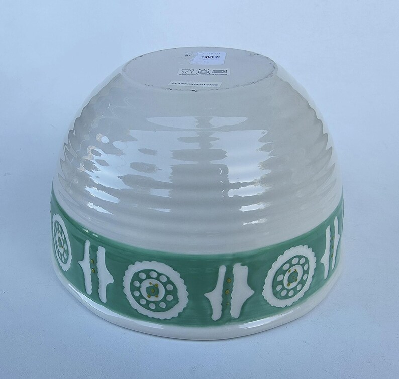 Peut inclure: Un bol en c&eacute;ramique blanc avec une bande verte orn&eacute;e d'un motif floral stylis&eacute; r&eacute;p&eacute;t&eacute;. Le bol a une texture c&ocirc;tel&eacute;e et une forme arrondie, adapt&eacute; au service ou &agrave; l'exposition.