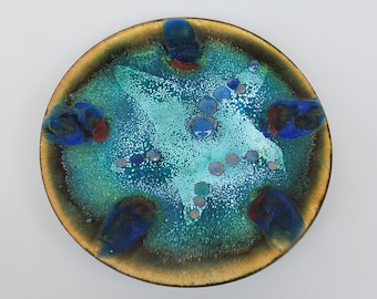 Könnte beinhalten: Eine runde Keramikschale mit einer blauen, grünen und goldenen Glasur. Die Schale hat eine gesprenkelte Textur und eine Vielzahl von blauen und weißen Punkten.