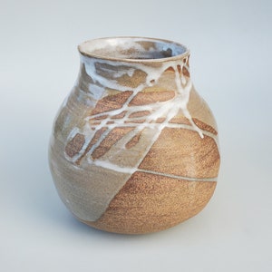 May include: A brown ceramic vase with white glaze and a textured surface. The vase has a rounded body and a wide opening.
