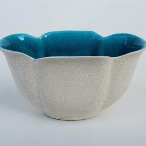 May include: A ceramic bowl with a crackle finish in off-white, featuring a vibrant teal interior. The bowl has a scalloped rim. This decorative piece is suitable for serving or display.