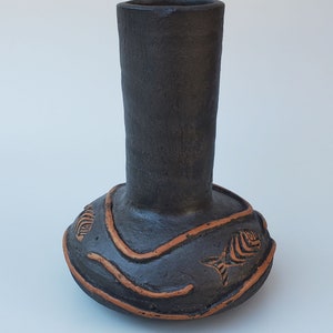 May include: A black ceramic vase with a wide base and a narrow neck. The vase is decorated with orange lines and fish designs.