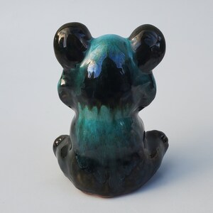 May include: A ceramic figurine of a black and teal bear sitting with its paws tucked in front of it.
