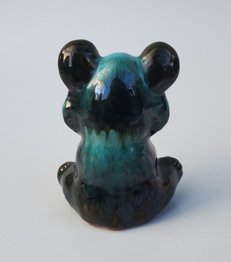 May include: A ceramic figurine of a black and teal bear sitting with its paws tucked in front of it.