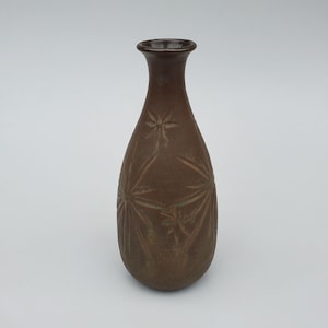 May include: A brown ceramic vase with a starburst design. The vase has a narrow neck and a rounded body.