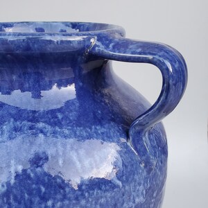 Op de afbeelding: Een grote, blauwe keramische vaas met twee handvatten. De vaas heeft een gemarmerd, getextureerd oppervlak en een glanzende afwerking.