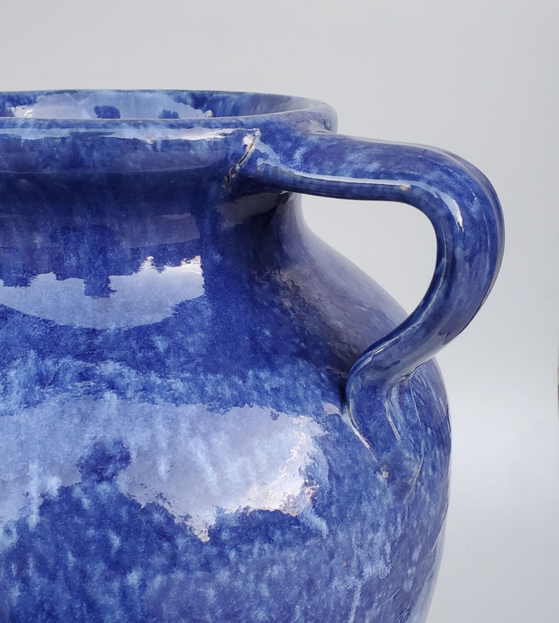 Op de afbeelding: Een grote, blauwe keramische vaas met twee handvatten. De vaas heeft een gemarmerd, getextureerd oppervlak en een glanzende afwerking.