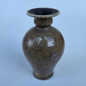 May include: A ceramic vase with a bulbous body and a wide, flat rim. The surface features a glossy, light brown glaze with a prominent dark crackle pattern throughout. The interior of the neck and the rim are finished in a dark, matte tone.