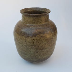 May include: A handcrafted, speckled ceramic vase with a wide, rounded body and a slightly flared rim. The vase has a mottled, earthy color palette of olive green and brown, with a textured surface. This decorative vase is suitable for displaying flowers or as a standalone art piece.