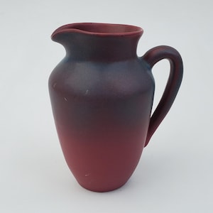 May include: A small, red and blue ceramic jug with a handle. The jug has a gradient colour scheme, fading from dark blue to red.
