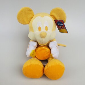 Puede incluir: Juguete de peluche amarillo de Mickey Mouse sosteniendo una pelota amarilla. El juguete tiene una cara blanca con ojos negros y una nariz negra. El juguete lleva una camisa blanca con rayas amarillas. El juguete tiene una etiqueta de Disney adherida a su oreja derecha.