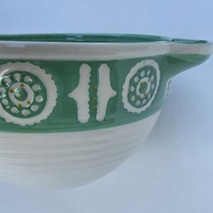 Peut inclure: Un saladier en c&eacute;ramique vert et blanc. Le bol est dot&eacute; d'une poign&eacute;e et est d&eacute;cor&eacute; de motifs floraux et g&eacute;om&eacute;triques blancs. Le bol a une finition brillante et une texture c&ocirc;tel&eacute;e sur la moiti&eacute; inf&eacute;rieure. Id&eacute;al pour la cuisine.