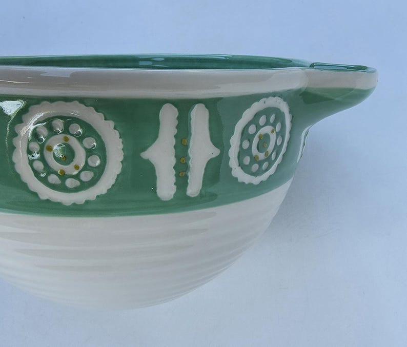 Peut inclure: Un saladier en c&eacute;ramique vert et blanc. Le bol est dot&eacute; d'une poign&eacute;e et est d&eacute;cor&eacute; de motifs floraux et g&eacute;om&eacute;triques blancs. Le bol a une finition brillante et une texture c&ocirc;tel&eacute;e sur la moiti&eacute; inf&eacute;rieure. Id&eacute;al pour la cuisine.