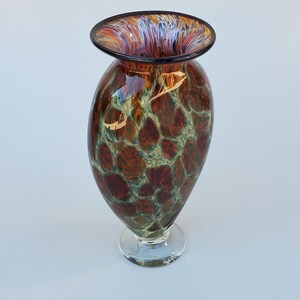 May include: A brown and green glass vase with a clear glass base. The vase has a mottled pattern and a wide, flared opening.