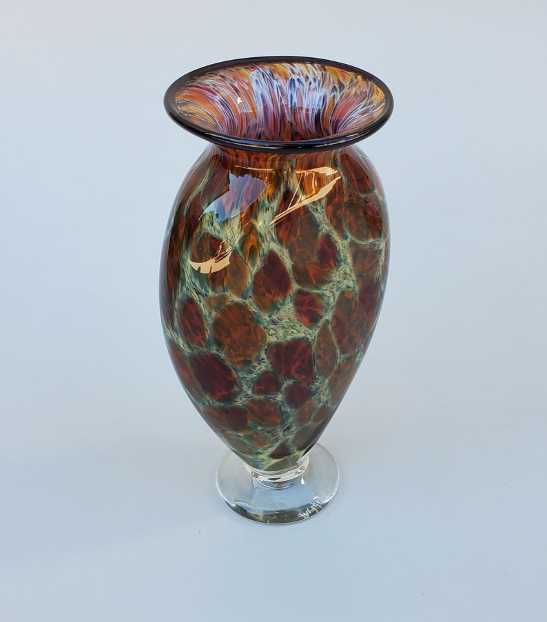 May include: A brown and green glass vase with a clear glass base. The vase has a mottled pattern and a wide, flared opening.