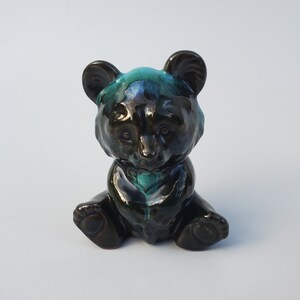 May include: A small ceramic bear figurine with a black and green glaze. The bear is sitting with its paws tucked in front of it.