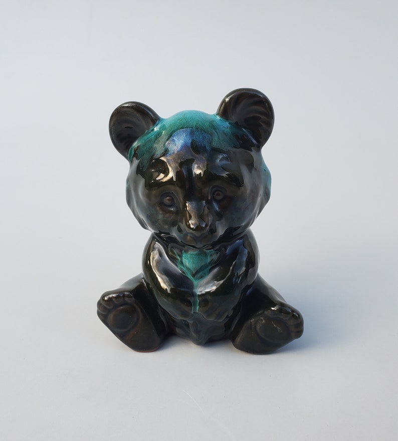 May include: A small ceramic bear figurine with a black and green glaze. The bear is sitting with its paws tucked in front of it.