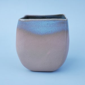 May include: A light pink ceramic planter with a light blue glaze on the top edge.