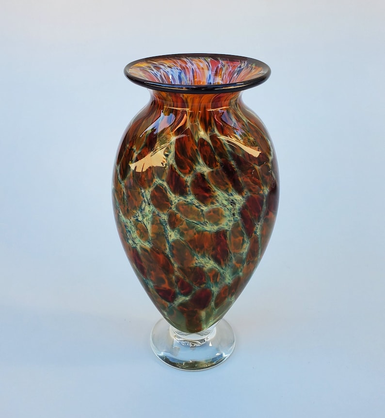 May include: A brown and green glass vase with a swirling pattern. The vase has a wide mouth and a narrow base.