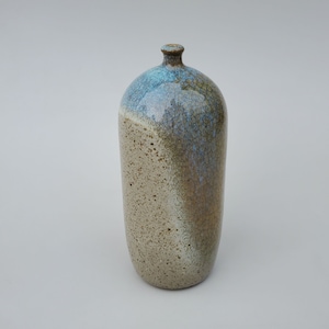 May include: A ceramic vase with a light brown, speckled glaze on the bottom half and a blue and brown glaze on the top half.
