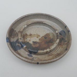 May include: A ceramic ashtray with a brown and white glaze and blue accents. The ashtray has a raised center ring.