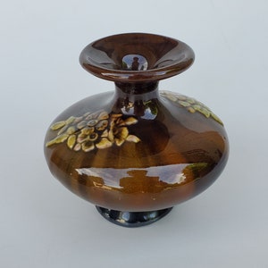 May include: A brown ceramic vase with a wide base and a narrow neck. The vase is decorated with raised floral designs in shades of green and yellow.