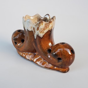 May include: A brown ceramic shoe-shaped planter with white glaze accents. The planter has multiple holes for drainage and is perfect for small plants.