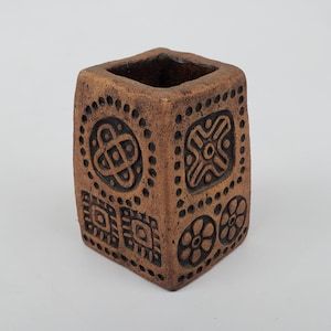 May include: A square ceramic planter with a brown glaze and black geometric designs. The planter has a square opening at the top.