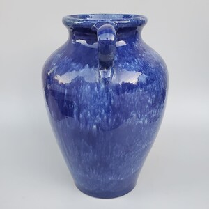 Op de afbeelding: Een blauwe keramische vaas met twee handvatten. De vaas heeft een gevlekt blauwe glazuur met witte strepen.