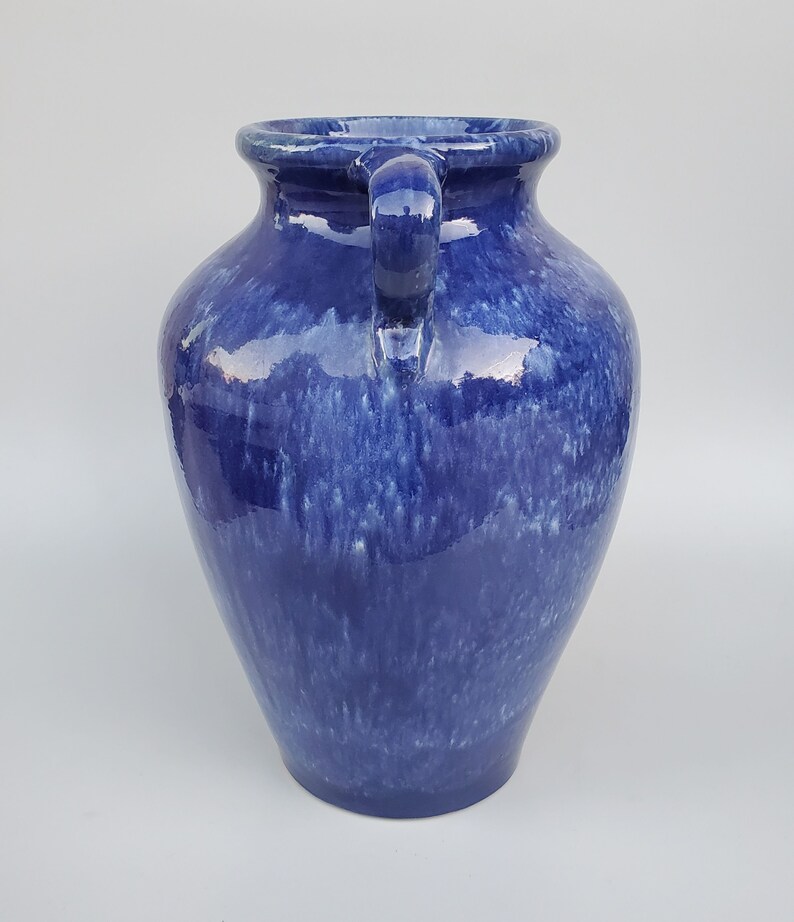 Op de afbeelding: Een blauwe keramische vaas met twee handvatten. De vaas heeft een gevlekt blauwe glazuur met witte strepen.