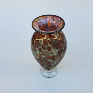 May include: A brown and green glass vase with a mottled pattern. The vase has a wide mouth and a narrow base. The vase is on a white background.