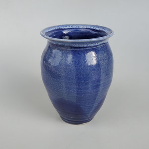 May include: A blue ceramic vase with a rounded body and a slightly flared rim. The vase has a light blue glaze with a subtle white speckling.