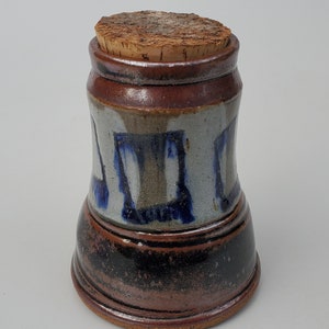 May include: A ceramic jar with a cork lid. The jar is decorated with blue and brown glaze and has a black base.