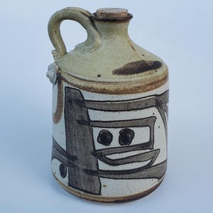 May include: A handmade ceramic jug with a handle and a cork stopper. The jug is beige with brown and black abstract designs. The jug has a unique, artistic appearance, suitable for decorative use or as a functional piece.