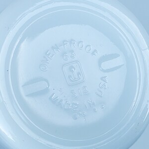 May include: Close-up of a light blue ceramic dish with the text "OVEN-PROOF 63" and "MADE IN USA" printed on the bottom. The dish has a small anchor symbol in a square.