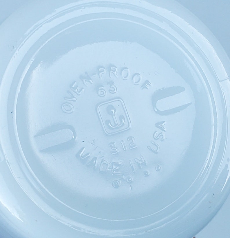 May include: Close-up of a light blue ceramic dish with the text "OVEN-PROOF 63" and "MADE IN USA" printed on the bottom. The dish has a small anchor symbol in a square.