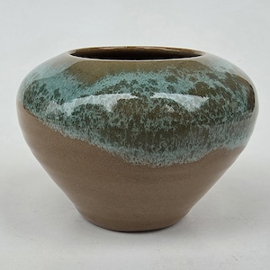 May include: A rounded ceramic vase with a smooth, matte brown base and a glossy, textured teal glaze dripping from the rim. The vessel features a wide, circular opening and a tapered bottom, showcasing a distinct contrast between the two finishes.