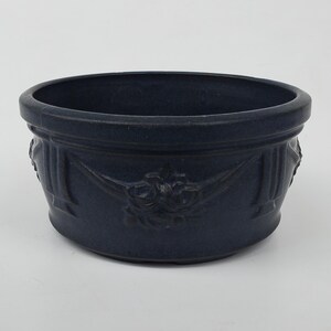 May include: A dark blue ceramic planter with a decorative floral design. The planter has a rounded shape and a wide rim.