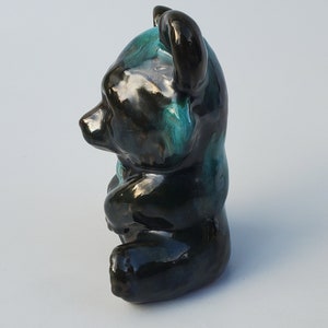 May include: A black and teal glazed ceramic bear figurine. The bear is sitting with its head tilted to the side.