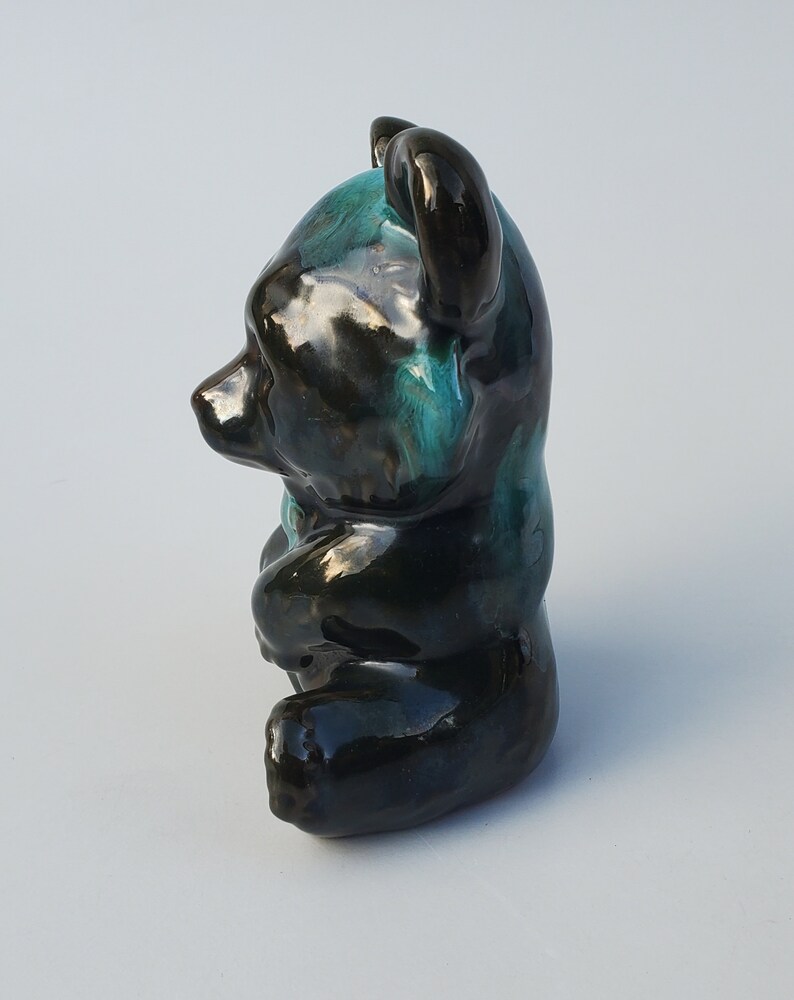 May include: A black and teal glazed ceramic bear figurine. The bear is sitting with its head tilted to the side.