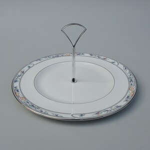 May include: A white ceramic cake stand with a floral design and a silver metal handle. The stand is perfect for serving desserts or snacks.