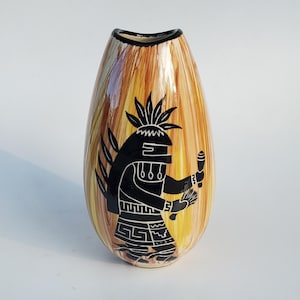 May include: A decorative, teardrop-shaped vase with a black and white Native American figure design. The vase has a textured, vertical striped pattern in shades of yellow, brown, and orange. The rim is black.
