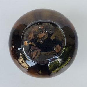 May include: A dark brown ceramic bowl with a glossy glaze. The bowl has a wide rim and a rounded bottom. The inside of the bowl is black with a mottled pattern.