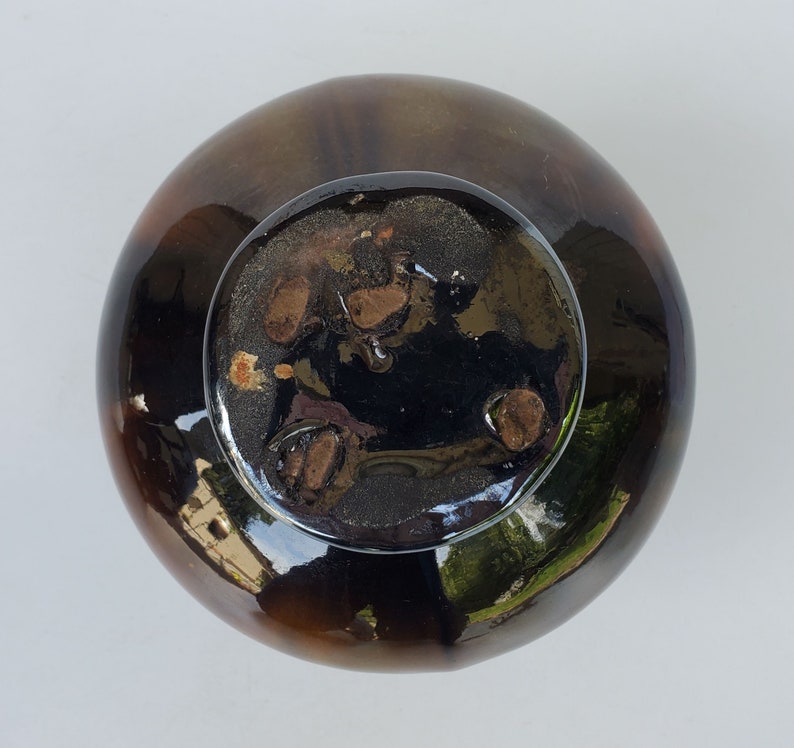 May include: A dark brown ceramic bowl with a glossy glaze. The bowl has a wide rim and a rounded bottom. The inside of the bowl is black with a mottled pattern.